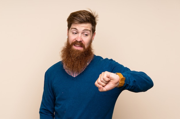 Homme rousse avec une longue barbe sur fond isolé à la recherche de la montre au poignet