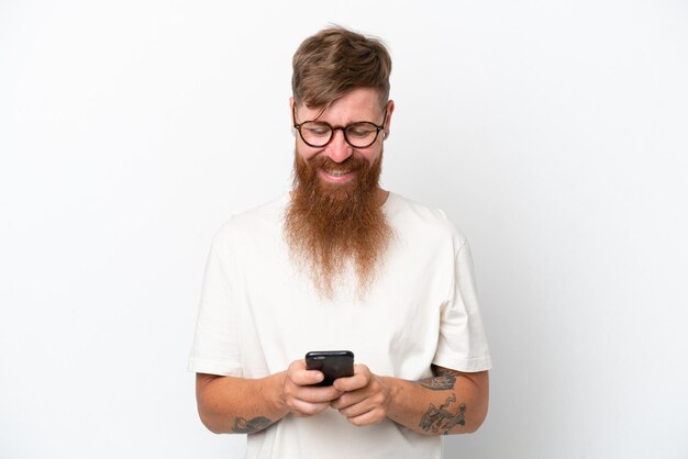 Homme rousse avec une longue barbe isolé sur fond blanc en envoyant un message avec le mobile