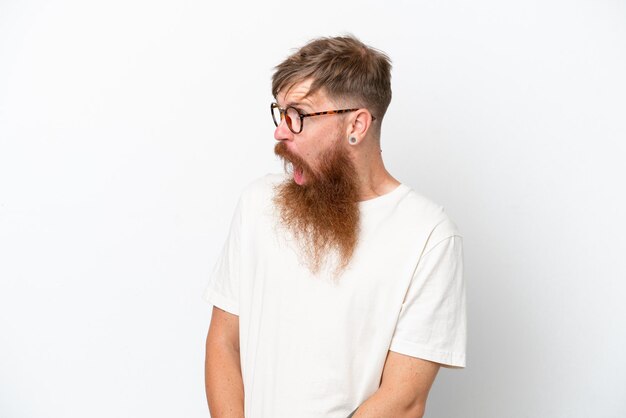 Homme rousse avec une longue barbe isolé sur fond blanc faisant un geste de surprise tout en regardant sur le côté