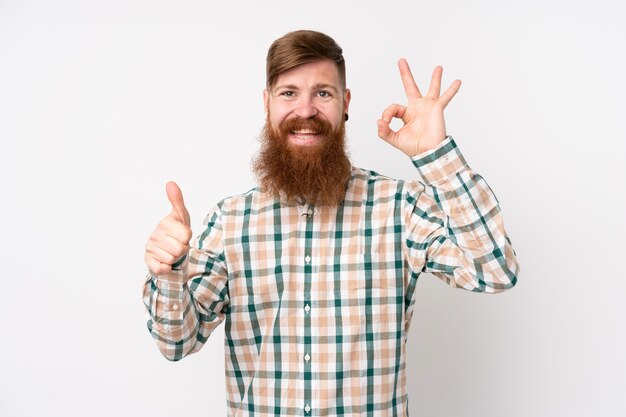 Homme rousse avec longue barbe sur mur blanc isolé montrant signe ok et geste du pouce vers le haut