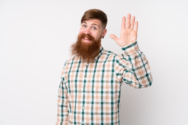 Homme rousse avec longue barbe sur mur blanc isolé saluant avec la main avec une expression heureuse