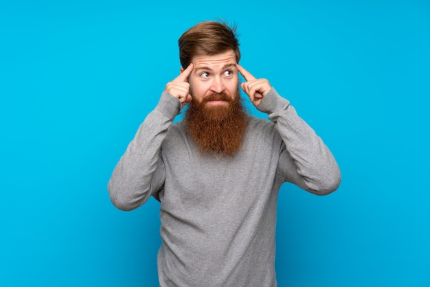 Homme rousse avec longue barbe sur mur bleu ayant des doutes et de la pensée