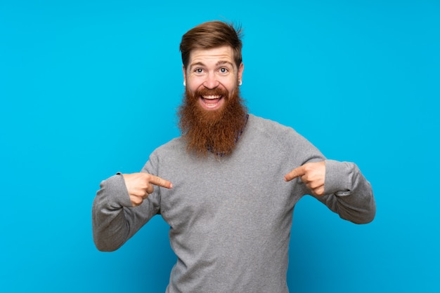 Homme rousse avec une longue barbe sur le mur bleu fier et satisfait de lui-même