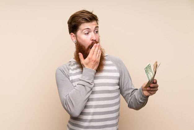 Homme rousse avec une longue barbe sur un mur isolé prenant beaucoup d'argent