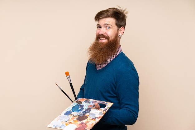 Homme rousse avec une longue barbe sur un mur isolé tenant une palette