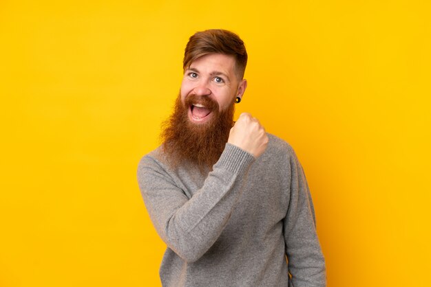 Homme rousse avec longue barbe sur mur jaune isolé célébrant une victoire