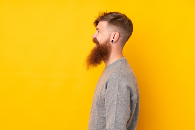 Homme rousse avec longue barbe sur mur jaune isolé à la recherche de côté