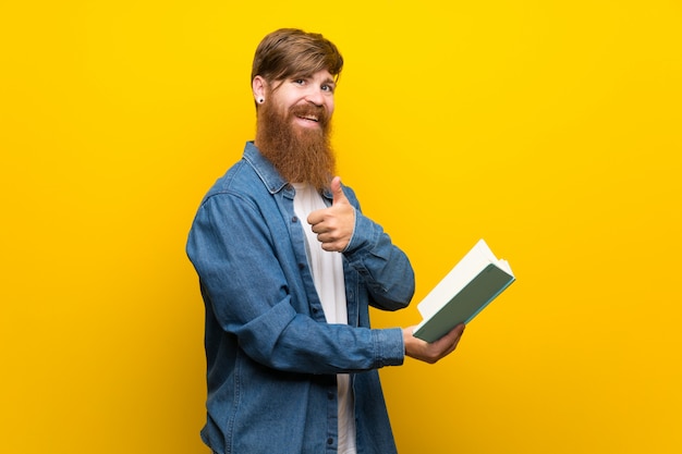 Homme rousse avec une longue barbe sur le mur jaune isolé tenant et en lisant un livre