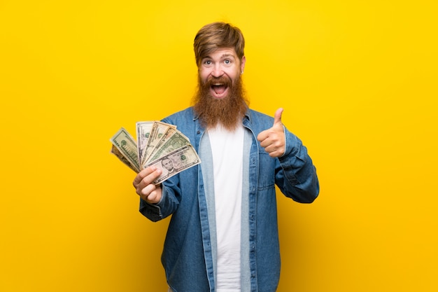 Homme rousse avec une longue barbe sur un mur jaune prenant beaucoup d'argent