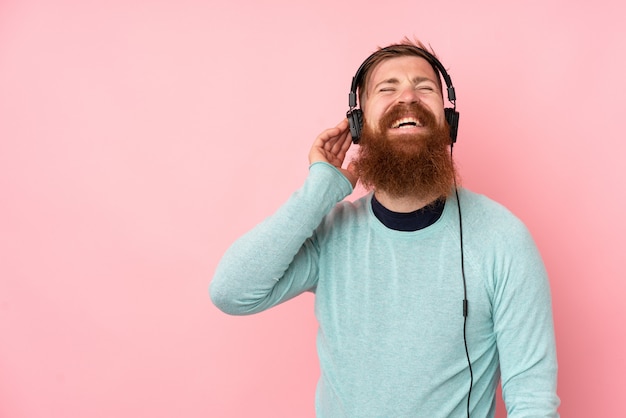 Homme rousse avec une longue barbe sur le mur rose isolé écouter de la musique et chanter