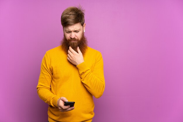 Homme rousse avec longue barbe sur mur violet penser et envoyer un message