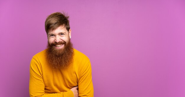 Homme rousse avec longue barbe sur mur violet souriant beaucoup