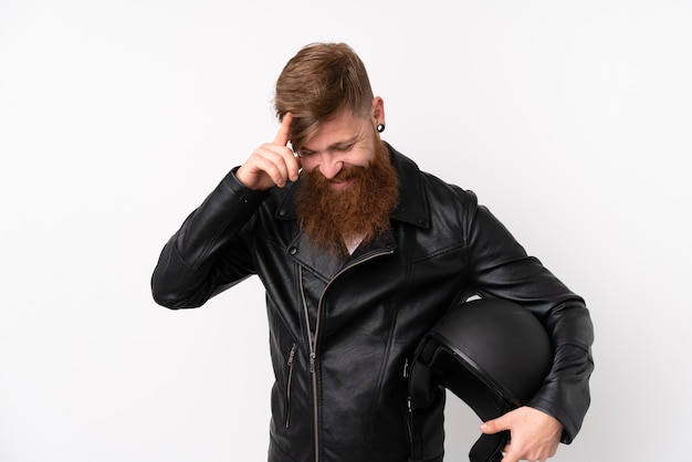 Homme rousse à longue barbe tenant un casque de moto sur un mur blanc en riant