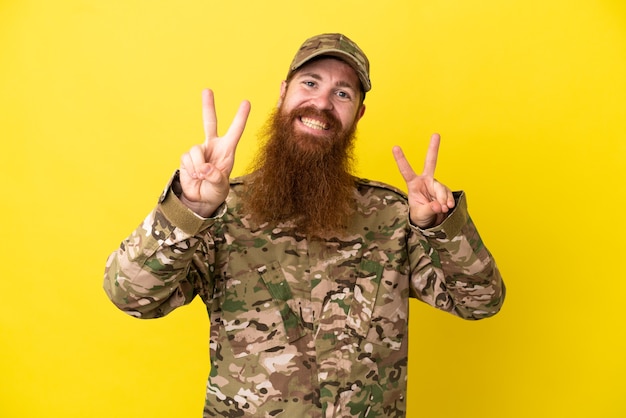 Homme rousse militaire sur isolé sur fond jaune montrant le signe de la victoire avec les deux mains