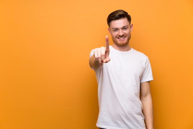 Homme rousse sur un mur brun montrant et en soulevant un doigt