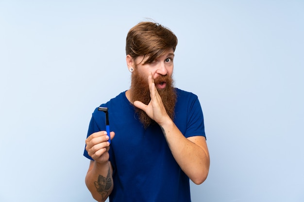 Homme rousse se rasant la barbe sur un mur bleu murmurant quelque chose