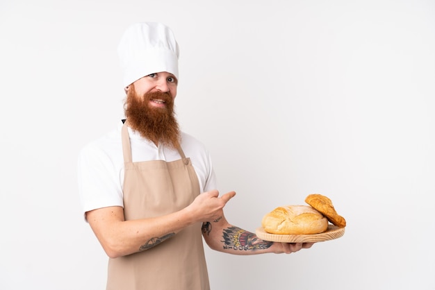 Homme rousse en uniforme de chef. Boulanger mâle tenant une table avec plusieurs pains et en le pointant