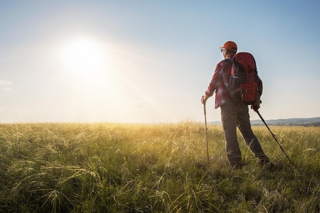 Homme routard randonnée dans le pré au coucher du soleil