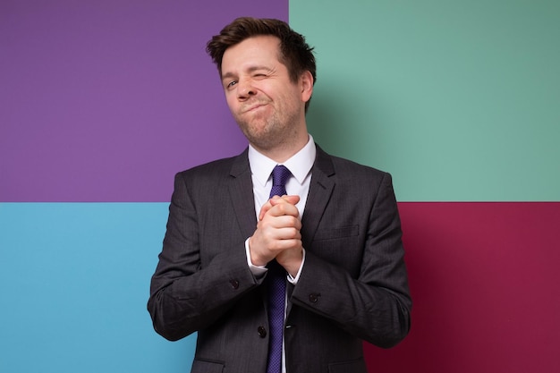 Un homme rusé en costume fait une grimace garde les paumes ensemble le gars a un bon plan pour réaliser Studio shot