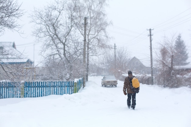 Un homme rustique marche dans la rue en hiver avec un sac à dos jaune. Tempête de neige