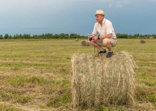 Un homme s'accroupit sur une balle de foin dans un champ