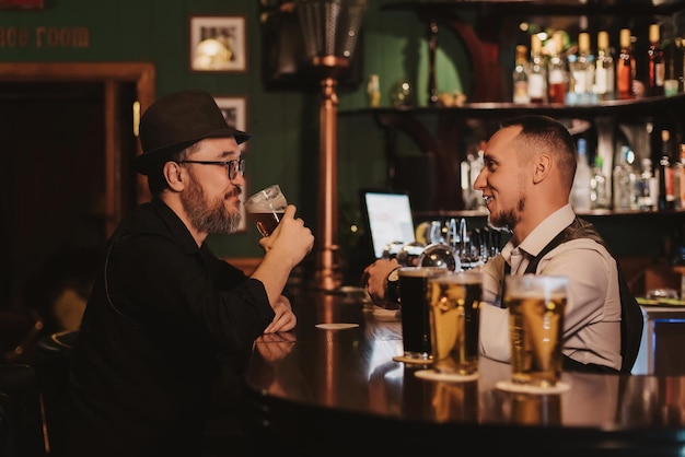 L'homme s'amuse à discuter avec un barman au comptoir du bar tout en buvant de la bière dans un verre