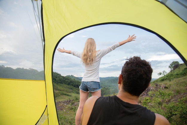 L'homme s'assied dans la tente et regarde sa petite amie se détendre parmi les belles montagnes