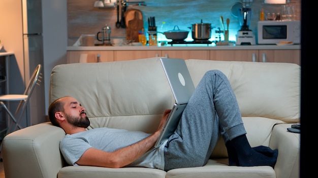 Homme s'endormant devant la télévision tout en travaillant sur l'ordinateur portable