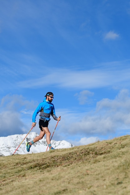 Un homme s'entraîne pour ultra run trail sur prairie vallonnée à l'automne avec la première neige sur les montagnes