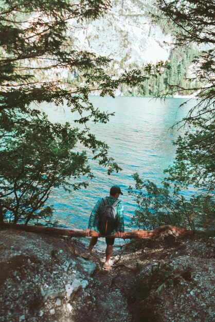 Homme avec sac à dos assis à bûche de bois profitant de la vue sur l'eau