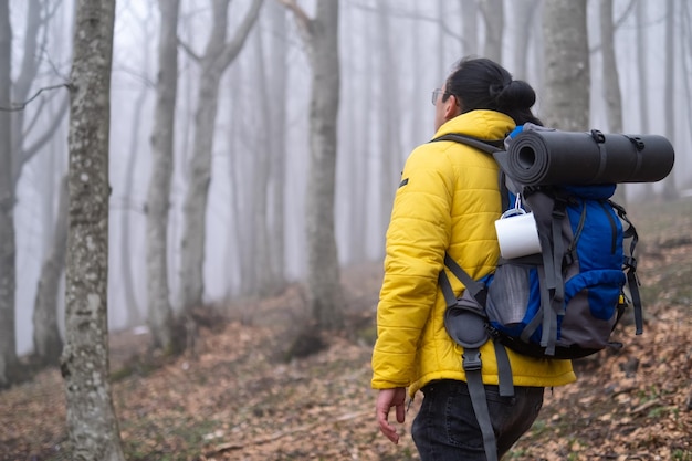 Homme avec sac à dos de camping marchant dans la forêt un jour brumeux