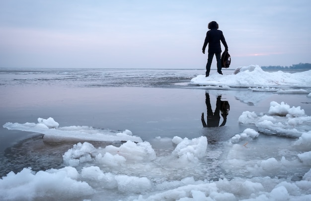 Homme avec sac à dos sur la côte de la rivière gelée au coucher du soleil. Notion de voyageur