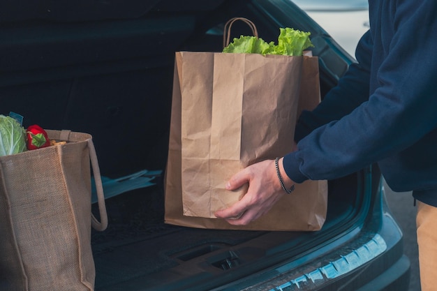 Un homme avec des sacs d'épicerie les met dans le coffre de la voiture.