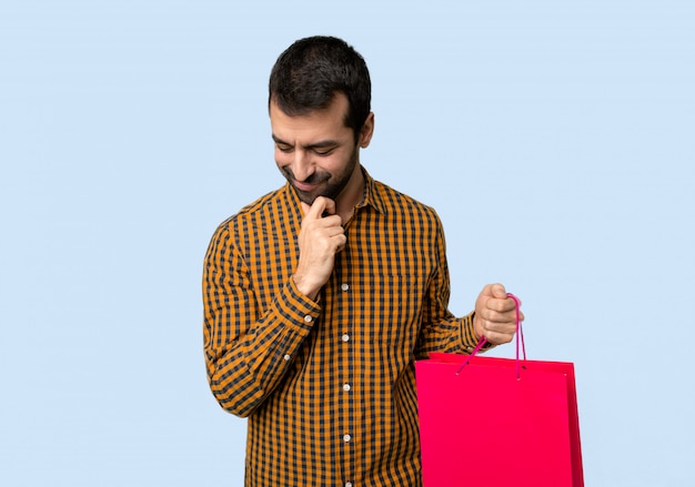 Homme avec des sacs à provisions en regardant avec la main sur le menton sur fond bleu isolé