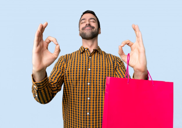 Homme avec des sacs à provisions en zen pose sur fond bleu isolé