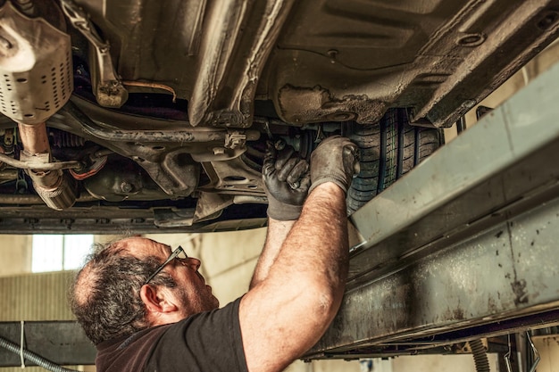 Homme sale debout dans un espace sous une voiture fixant l'alignement de la direction dans un atelier de mécanique