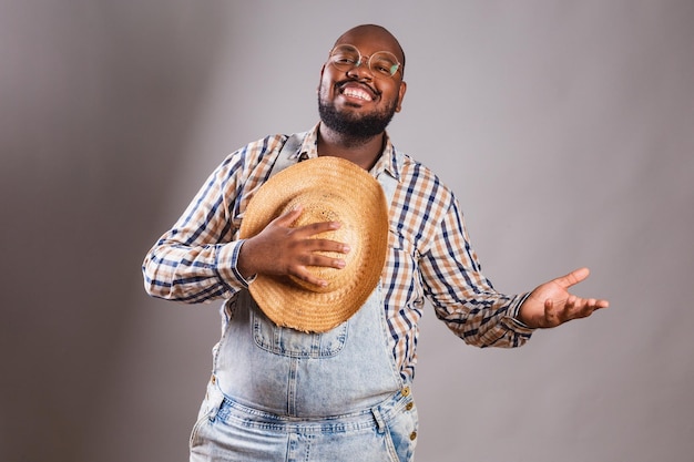 Un homme en salopette et chapeau de paille sourit et tient un chapeau de paille.