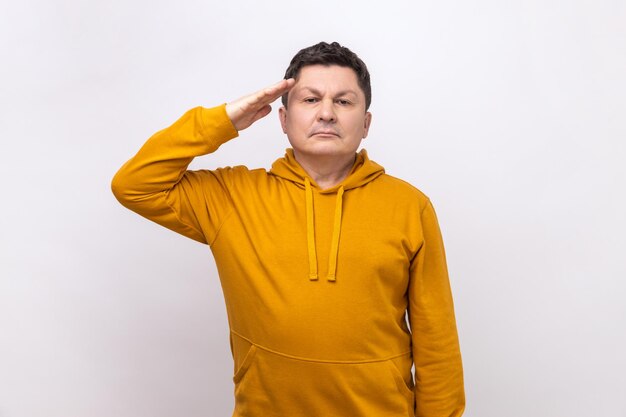 Homme saluant tenant la main près de la tête en regardant la caméra avec une expression sérieuse