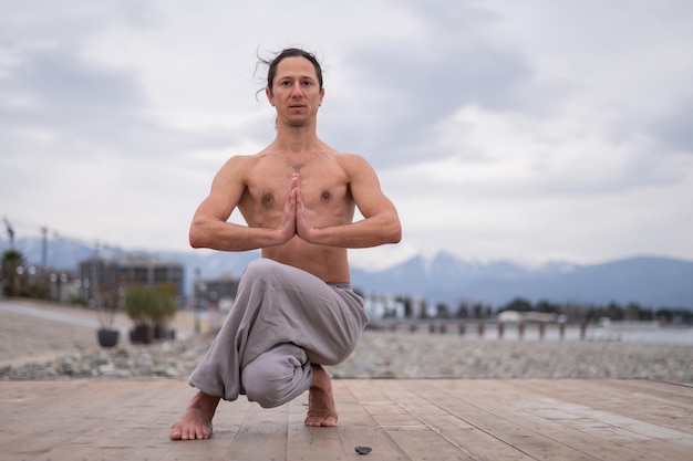 Un homme sans chemise fait du yoga sur la jetée.