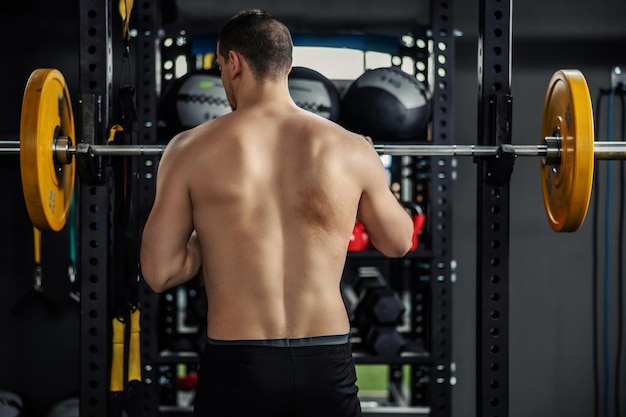 Un homme sans t-shirt se prépare à soulever une barre avec des poids dans la salle de sport