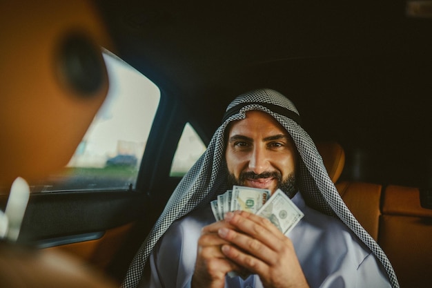 Homme saoudien en costume traditionnel dans une voiture tenant de l'argent