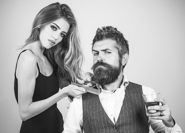 Homme satisfait buvant du whisky dans un salon de coiffure tandis que la styliste féminine sexy se rase avec un rasoir Lady joue