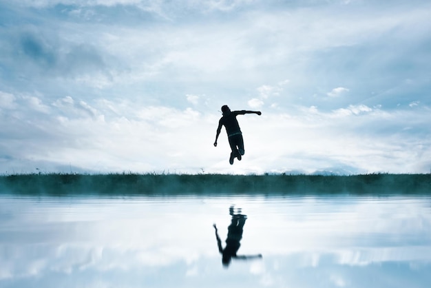 Photo un homme sautant dans le champ et réfléchissant dans le lac.