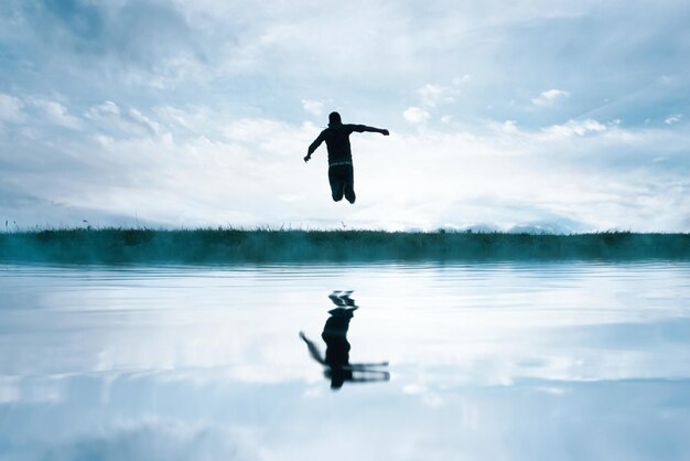 Un homme sautant dans le champ et réfléchissant dans le lac.