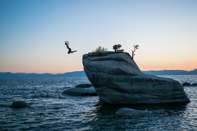 Photo un homme sautant d'un rocher par la mer contre un ciel clair