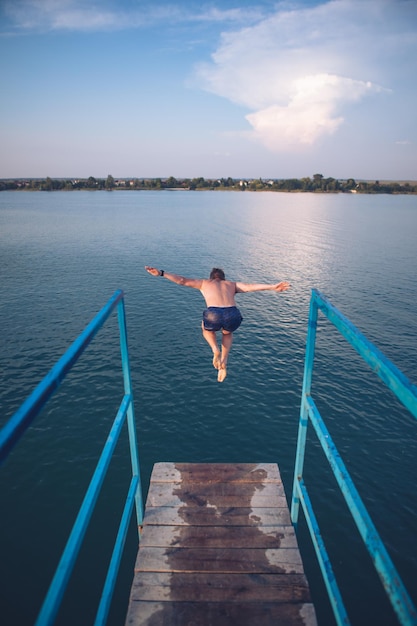 Homme sautant de la tour à l'eau du lac au coucher du soleil