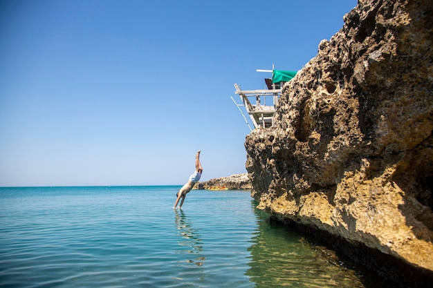 Photo un homme saute dans l'eau d'une falaise.