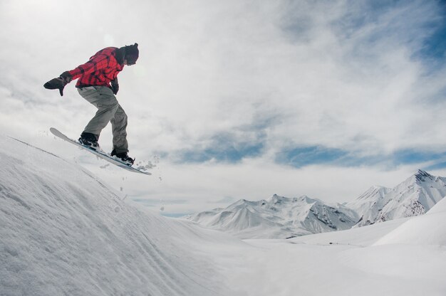 L'homme saute sur un snowboard contre un sommet enneigé