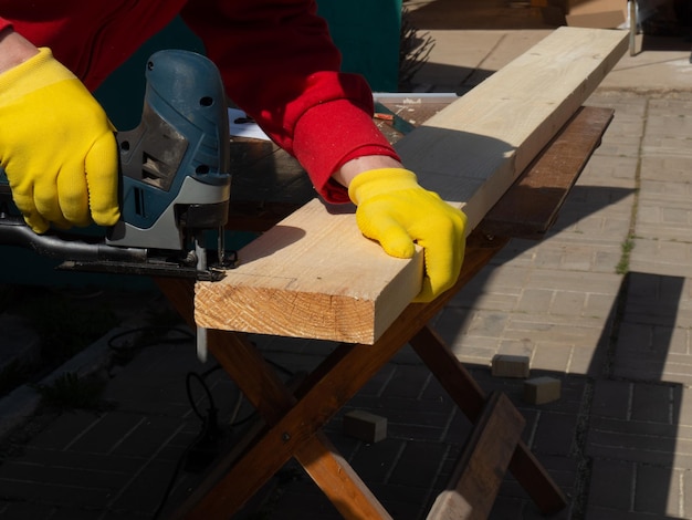 Un homme scie une planche avec une scie sauteuse électrique gros plan scie électrique à main le concept de travail avec du bois