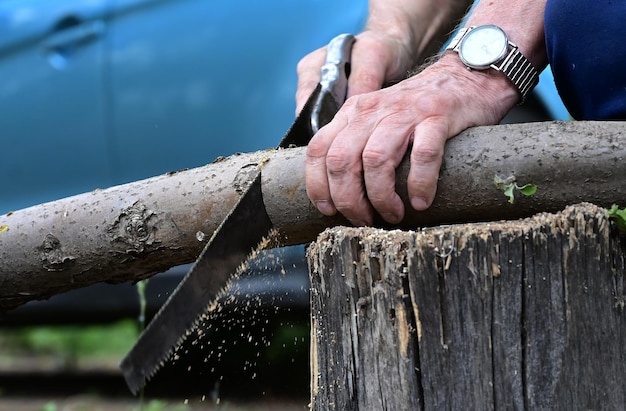 Un homme avec une scie scie une planche de bois Le concept de nettoyage dans la zone suburbaine